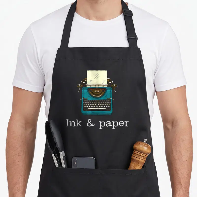 Tablier de cuisine noir avec une machine à écrire bleue et le texte Ink & paper en blanc.