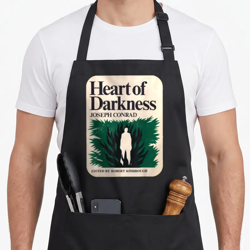 Tablier de cuisine noir avec illustration de couverture de livre Heart of Darkness et silhouette blanche dans la végétation verte.