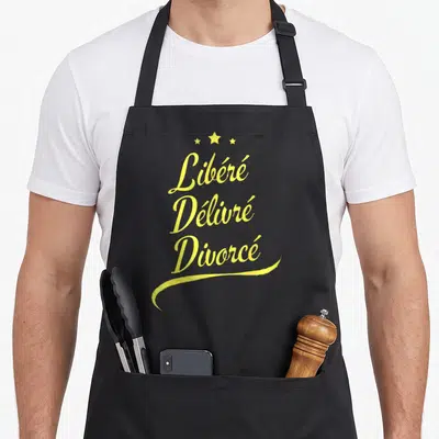 Tablier de cuisine noir avec linscription Libéré Délivré Divorcé en lettres jaunes cursives et trois étoiles au sommet.