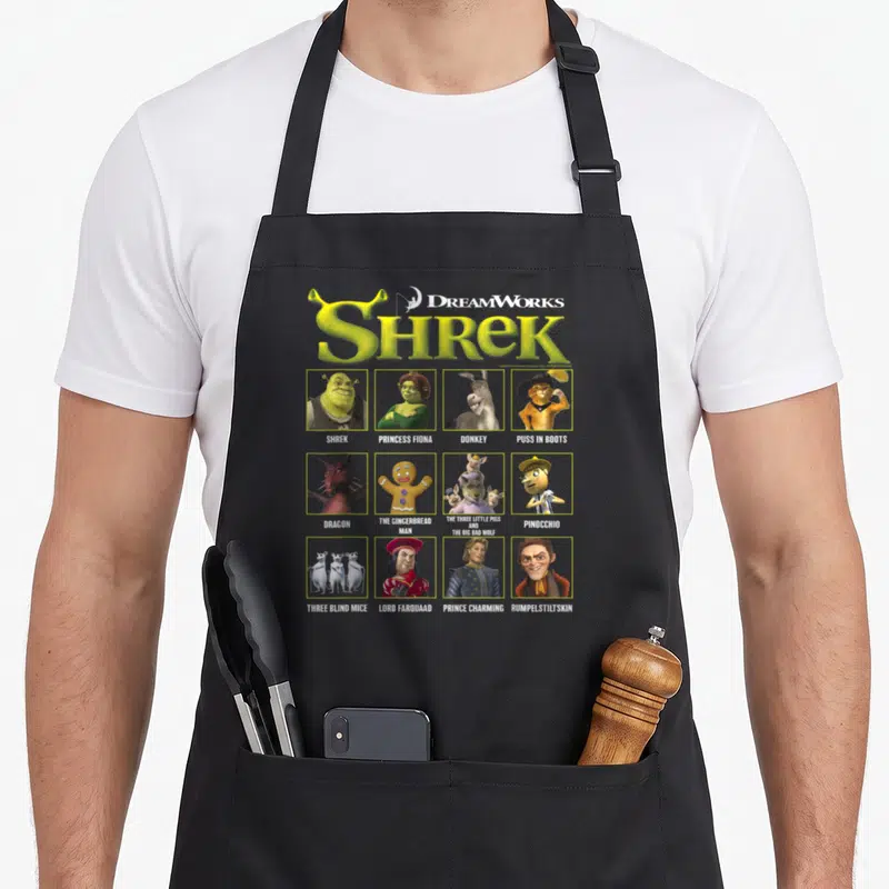Tablier de cuisine noir avec le logo Shrek et douze portraits de personnages encadrés en grille.