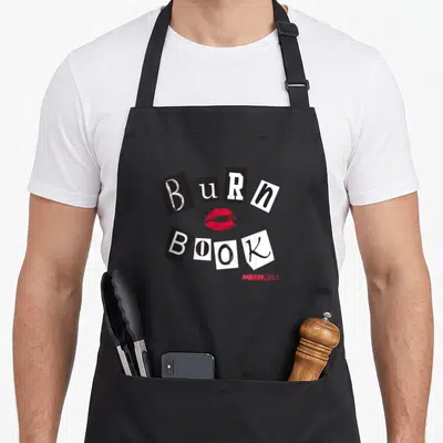 Tablier de cuisine noir avec motif collage Burn Book et trace de lèvres rouges.