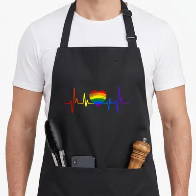 Tablier de cuisine noir avec un cœur arc-en-ciel traversé par une ligne de rythme cardiaque multicolore.
