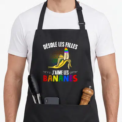 Tablier de cuisine noir avec une banane pelée aux couleurs de l'arc-en-ciel et un texte humoristique en blanc et multicolore.
