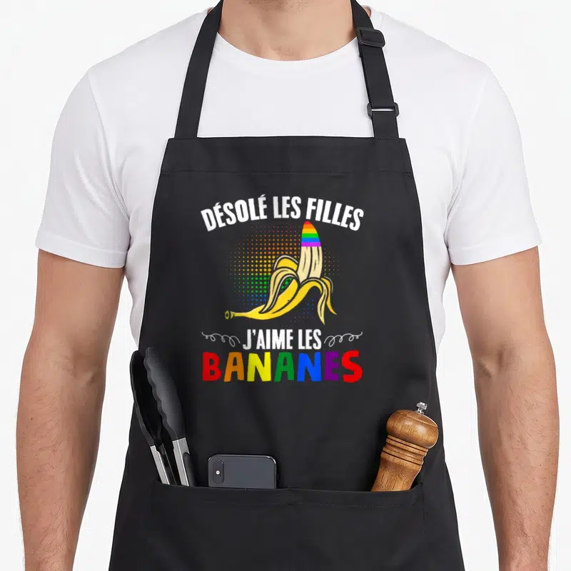 Tablier de cuisine noir avec une banane pelée aux couleurs de l'arc-en-ciel et un texte humoristique en blanc et multicolore.
