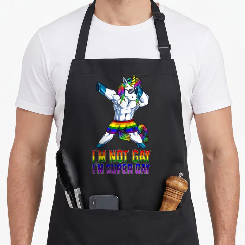 Tablier de cuisine noir avec licorne musclée aux couleurs de l'arc-en-ciel et texte humoristique.