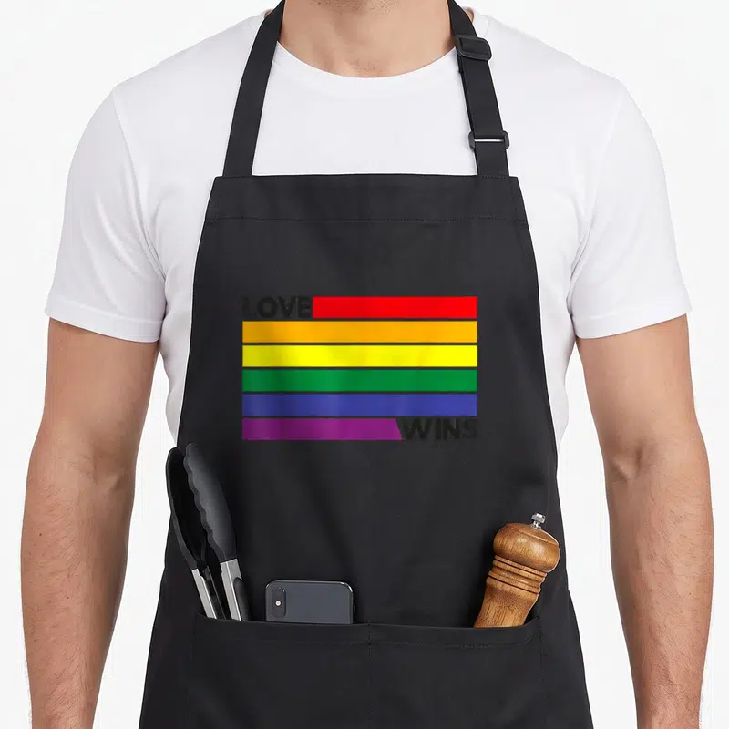Tablier de cuisine noir avec les mots Love Wins et des bandes colorées arc-en-ciel.