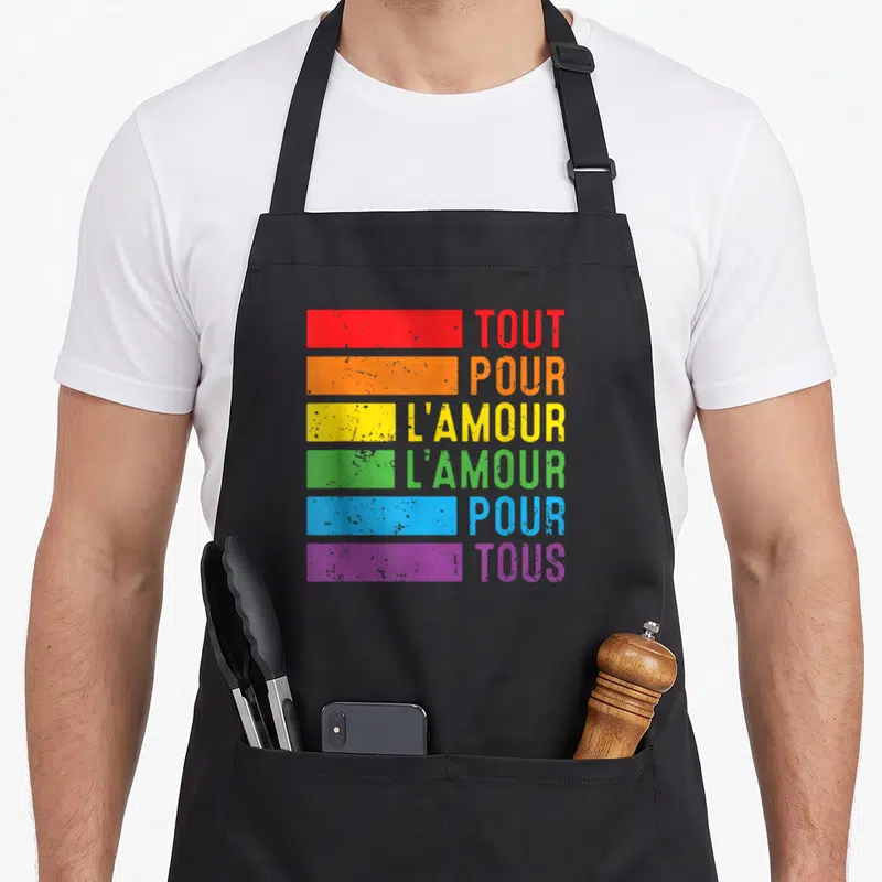 Tablier de cuisine noir avec bandes colorées arc-en-ciel et texte Tout Pour L'Amour pour Tous imprimé en gras.