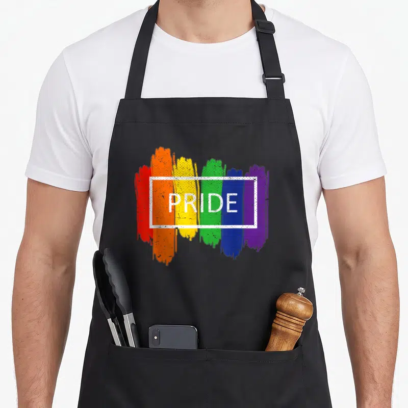 Tablier de cuisine noir avec arc-en-ciel aux touches de peinture rouge orange jaune vert bleu violet et le mot PRIDE en blanc au centre.