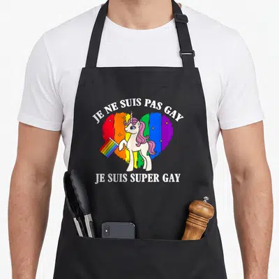 Tablier de cuisine noir avec une licorne tenant un drapeau devant un cœur arc-en-ciel et du texte blanc.