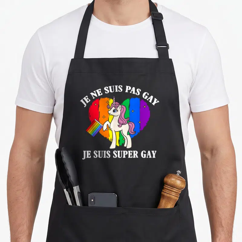 Tablier de cuisine noir avec une licorne tenant un drapeau devant un cœur arc-en-ciel et du texte blanc.