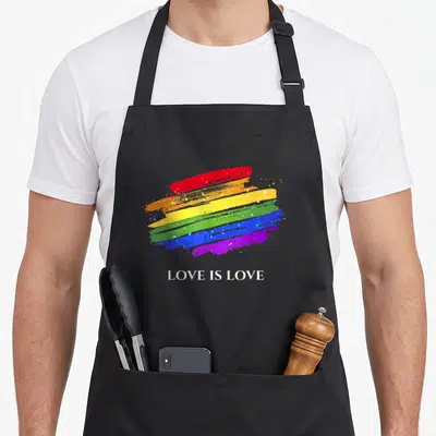 Tablier de cuisine noir avec un drapeau arc-en-ciel stylisé et l'inscription Love Is Love en bas.