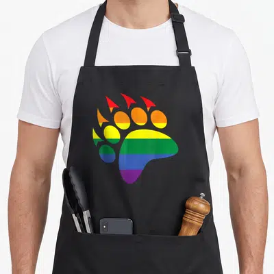 Tablier de cuisine noir avec une grande patte d'ours aux couleurs vives de l'arc-en-ciel imprimée sur le devant.