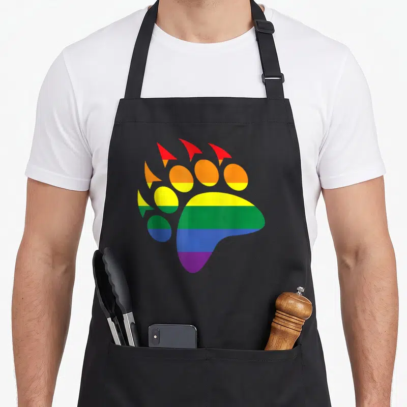Tablier de cuisine noir avec une grande patte d'ours aux couleurs vives de l'arc-en-ciel imprimée sur le devant.