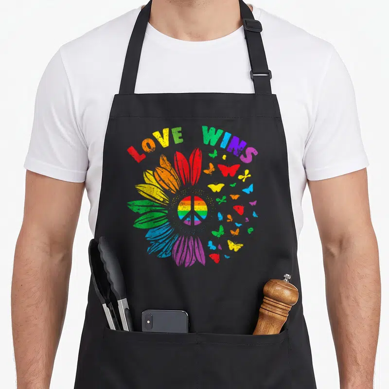 Tablier de cuisine noir avec Love Wins, tournesol arc-en-ciel, signe de paix et papillons multicolores.