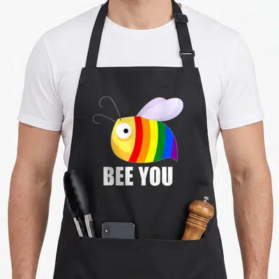 Tablier de cuisine noir avec une abeille aux bandes arc-en-ciel et le texte Be You Bee en blanc