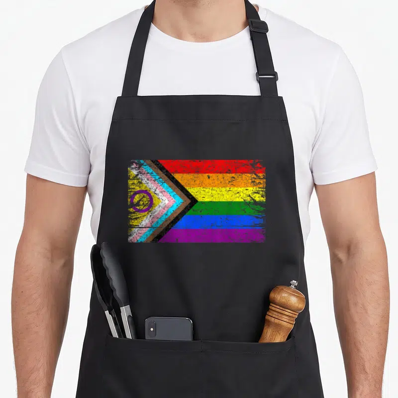 Tablier de cuisine noir avec le motif Progress Pride Flag incluant le cercle intersex et les bandes colorées distinctives.