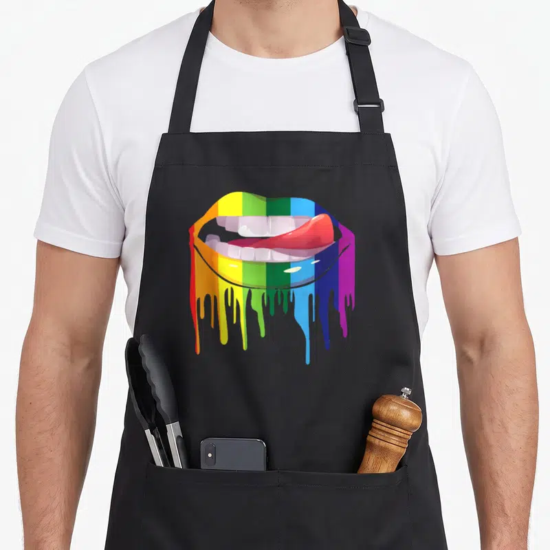 Tablier de cuisine noir avec une illustration de bouche aux lèvres arc-en-ciel dont la couleur coule sur le côté droit.