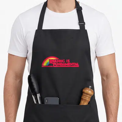 Tablier de cuisine noir avec inscription rouge Reading Is Fundamental et arc en ciel multicolore stylisé.
