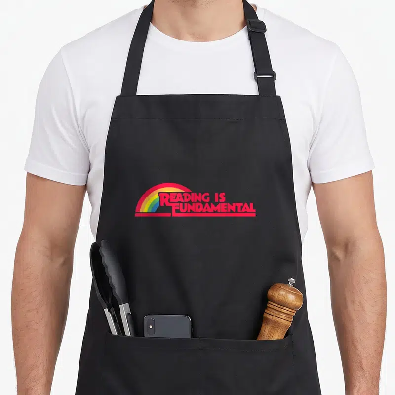 Tablier de cuisine noir avec inscription rouge Reading Is Fundamental et arc en ciel multicolore stylisé.