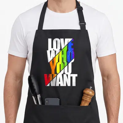 Tablier de cuisine noir avec texte Love Who You Want en blanc et diagonale aux couleurs de l'arc-en-ciel.