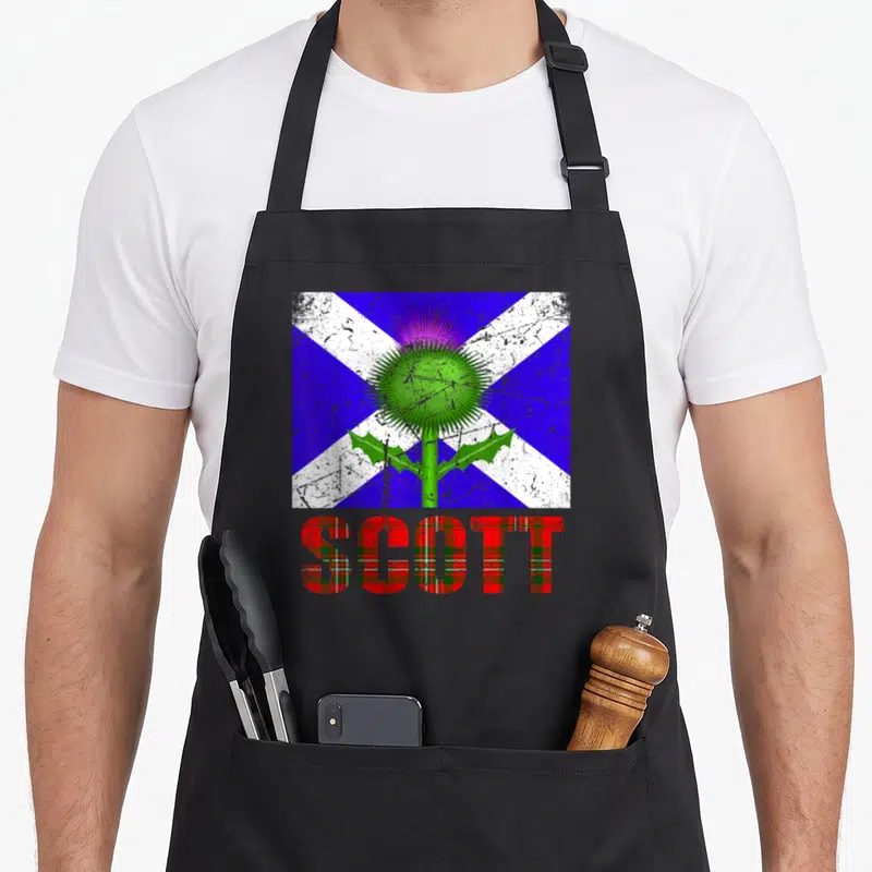 Tablier de cuisine noir avec drapeau écossais, thistle vert et inscription SCOTT en motif tartan rouge.