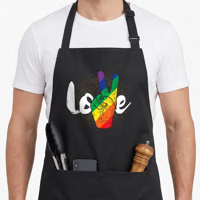 Tablier de cuisine noir avec une main rainbow faisant un signe de paix et le mot Love écrit en blanc.