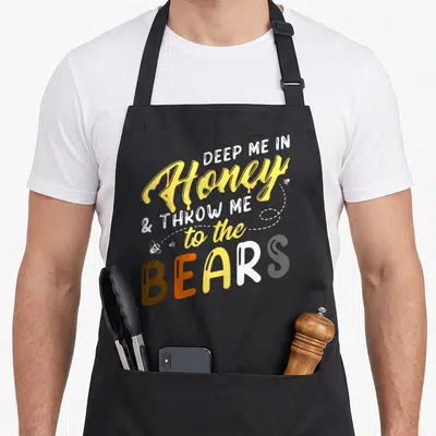 Tablier de cuisine noir avec inscription Deep Me in Honey to the Bears en jaune et blanc.