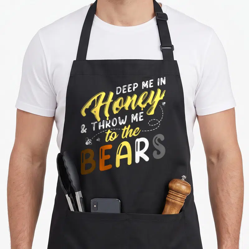 Tablier de cuisine noir avec inscription Deep Me in Honey to the Bears en jaune et blanc.