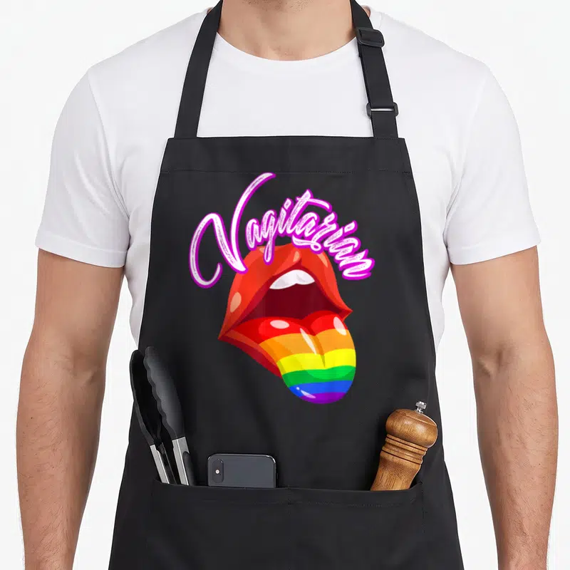 Tablier de cuisine noir avec illustration de lèvres rouges et langue aux couleurs de l'arc-en-ciel sous une inscription rose.