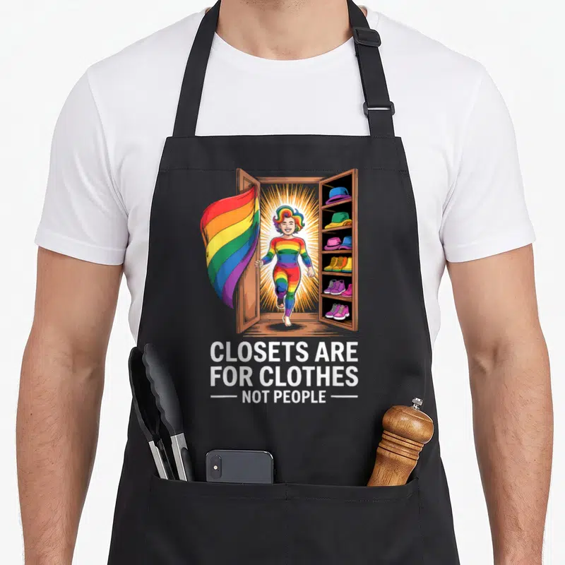 Tablier de cuisine noir avec une personne arc-en-ciel sortant d'une armoire et un drapeau LGBT flottant.