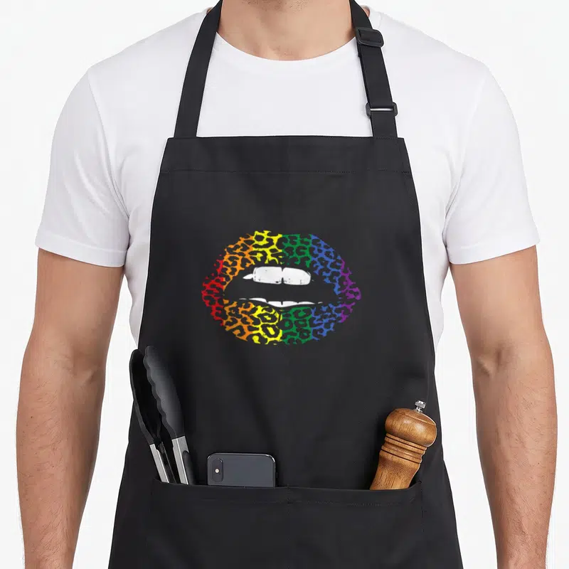 Tablier de cuisine noir avec lèvres arc-en-ciel et motif léopard coloré au centre.