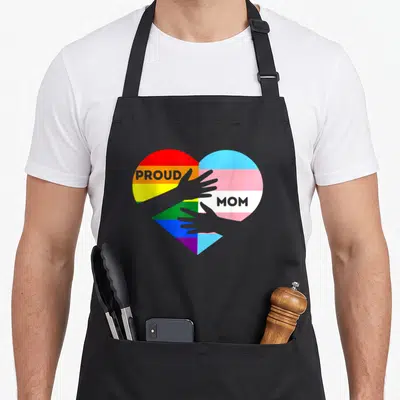 Tablier de cuisine noir avec un cœur aux couleurs du drapeau rainbow et transgenre tenant deux mains grises.