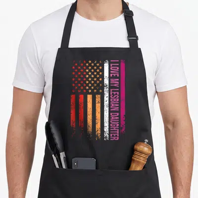 Tablier de cuisine noir avec un drapeau stylisé rose orange et blanc portant l'inscription I love my lesbian daughter en vertical.