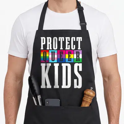 Tablier de cuisine noir avec le texte Protect Queer Kids et des drapeaux arc-en-ciel multicolores au centre.