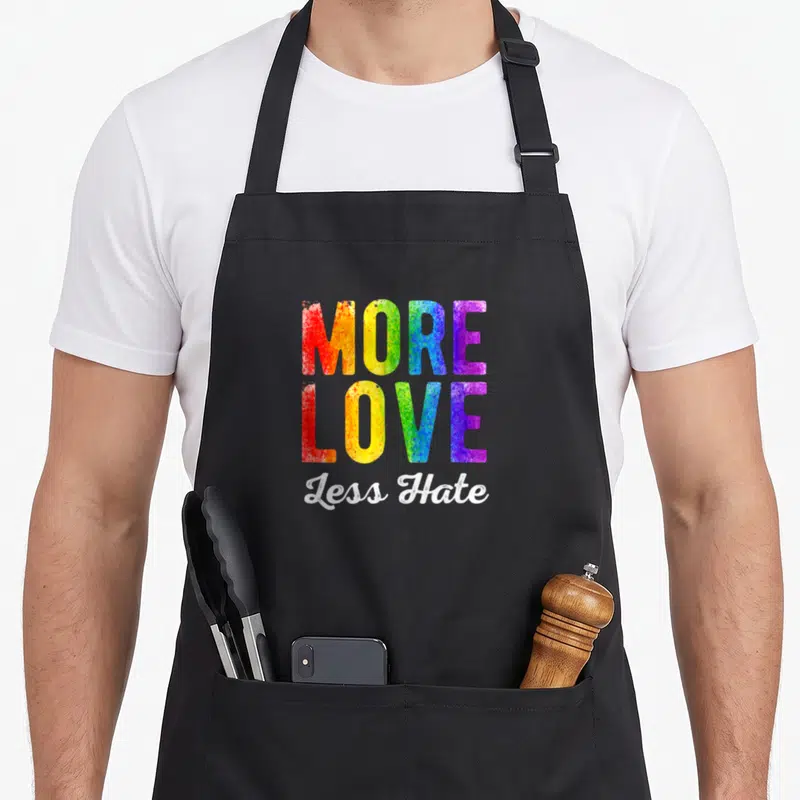 Tablier de cuisine noir avec inscription More Love Less Hate aux couleurs de l'arc-en-ciel et du blanc.