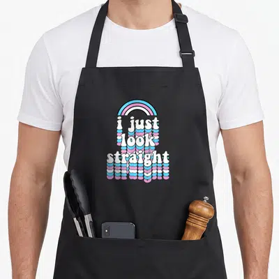 Tablier de cuisine noir avec le texte i just look straight en lettres gonflées multicolores sur fond gris uni.