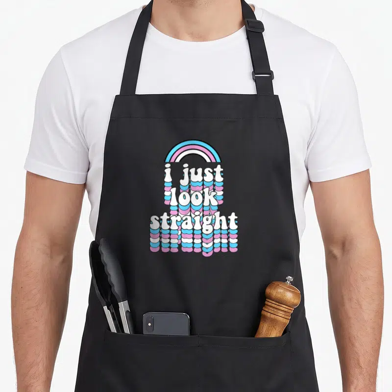 Tablier de cuisine noir avec le texte i just look straight en lettres gonflées multicolores sur fond gris uni.