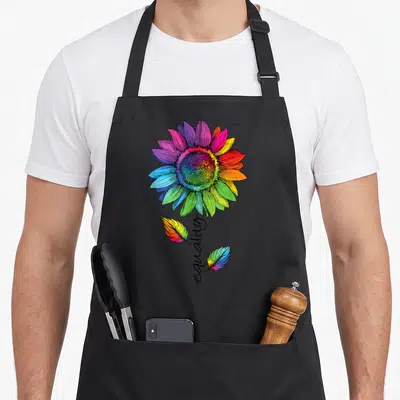 Tablier de cuisine noir avec une grande fleur aux pétales multicolores et le mot equality en calligraphie noire sur la tige.