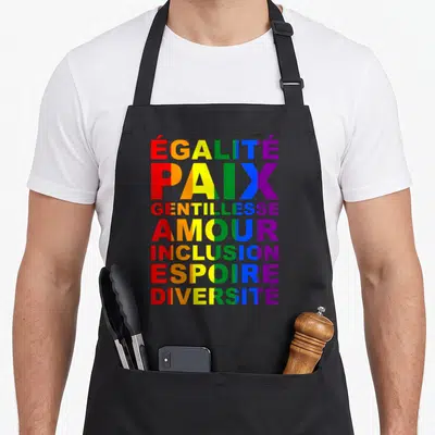 Tablier de cuisine noir avec les mots Égalité Paix Amour Gentillesse Inclusion Espoir Diversité en lettres arc-en-ciel.