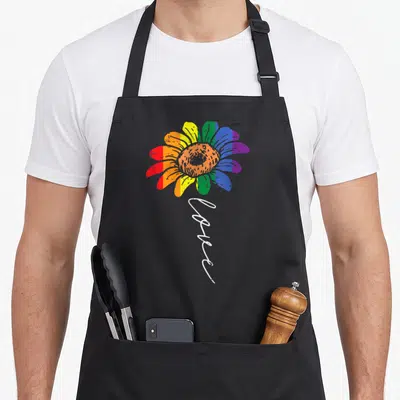 Tablier de cuisine noir avec un grand tournesol aux couleurs de l'arc-en-ciel et le mot Love en blanc sous la fleur.