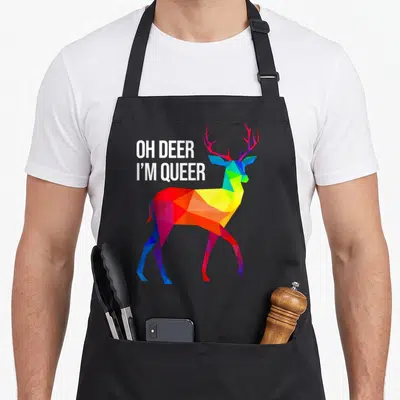 Tablier de cuisine noir avec un cerf géométrique aux couleurs de l'arc-en-ciel et le texte Oh Deer I'm Queer en blanc.