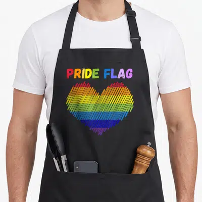 Tablier de cuisine noir avec un cœur arc-en-ciel stylisé et le texte PRIDE FLAG en lettres colorées.
