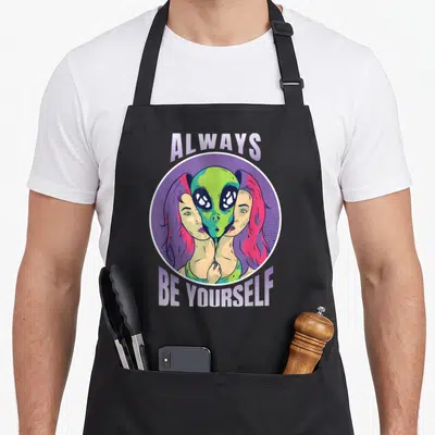 Tablier de cuisine noir avec illustration circulaire Always Be Yourself et alien vert au centre.