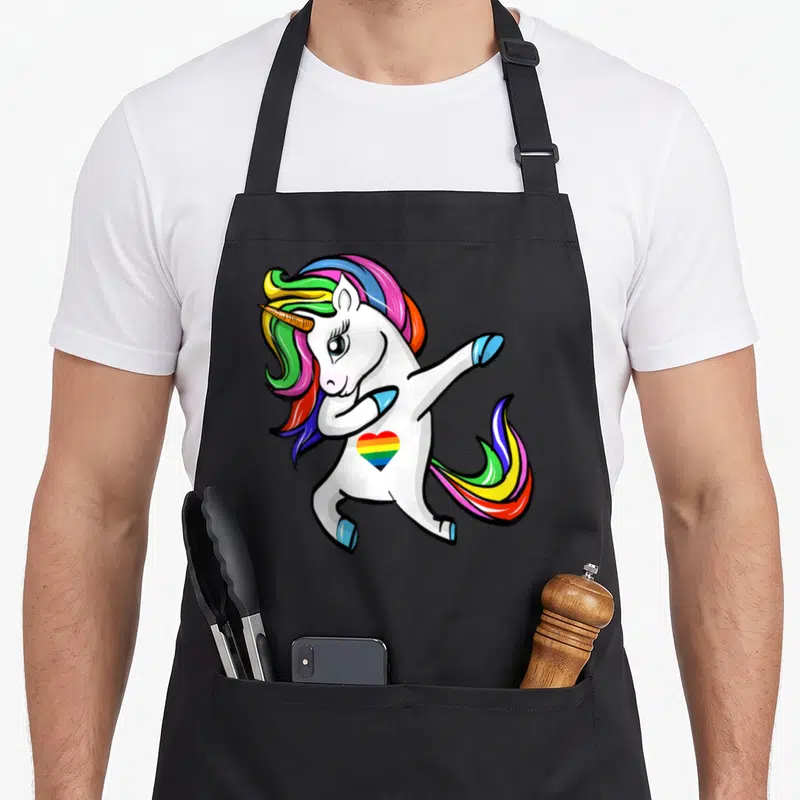 Tablier de cuisine noir avec une licorne blanche effectuant un dab et un cœur aux couleurs de l'arc-en-ciel sur la poitrine.