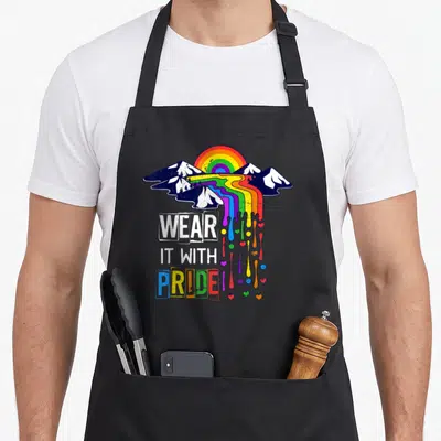 Tablier de cuisine noir avec illustration arc-en-ciel fondant sur montagnes et texte « Portez-le avec fierté » multicolore.