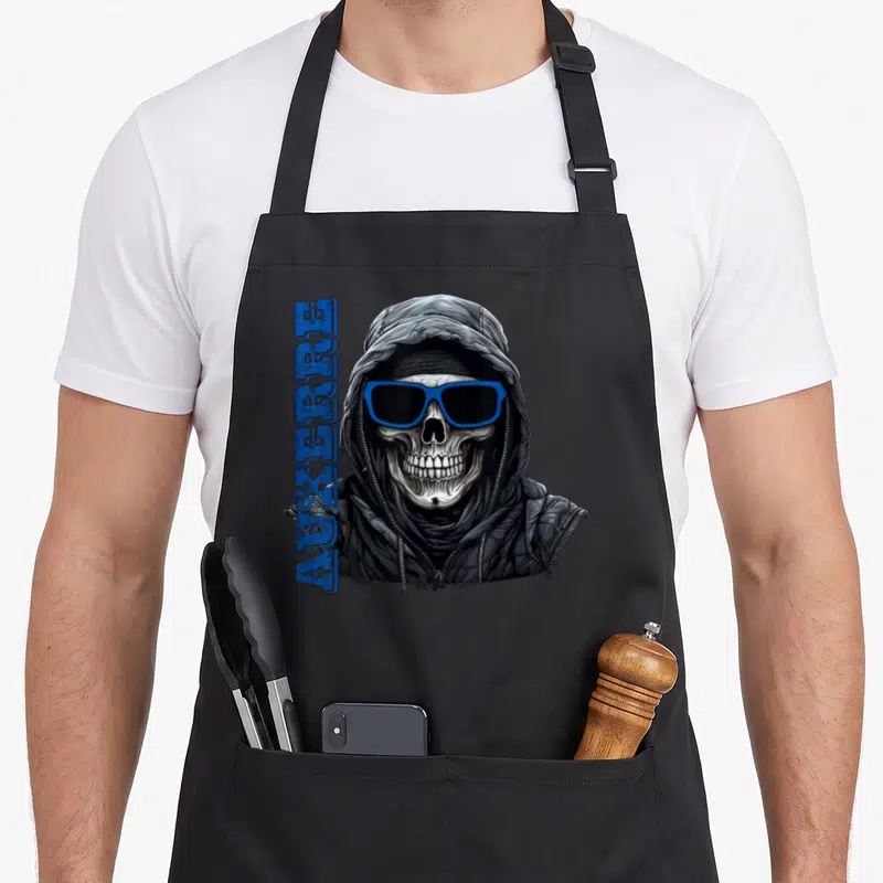 Tablier de cuisine noir avec un crâne en capuche portant des lunettes bleues et le mot Auxerre imprimé verticalement.