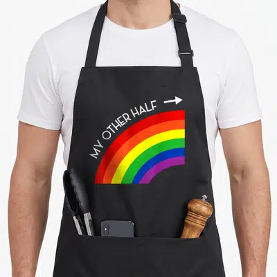Tablier de cuisine noir avec un arc en ciel multicolore et le texte My Other Half suivi d'une flèche blanche.