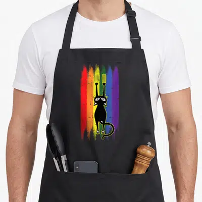 Tablier de cuisine noir avec un chat noir tenant une fourche et un griffoir sur fond de bandes colorées rainbow.