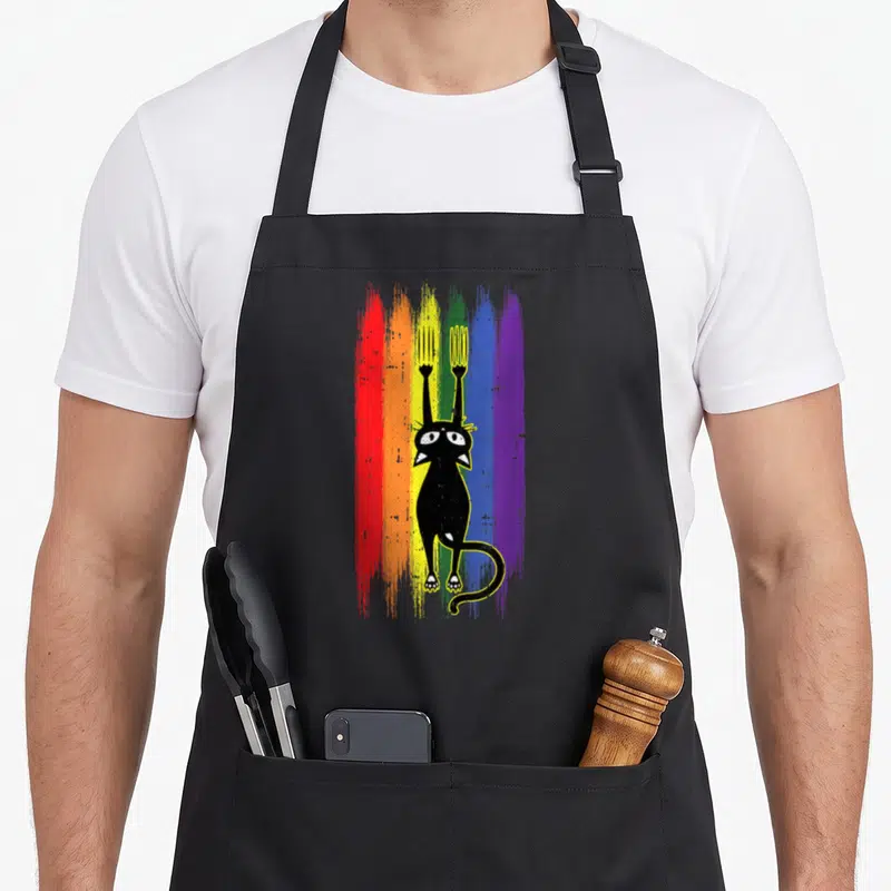 Tablier de cuisine noir avec un chat noir tenant une fourche et un griffoir sur fond de bandes colorées rainbow.