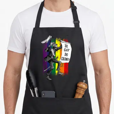 Tablier de cuisine noir avec illustration d'un squelette en costume tenant une banderole Be Gay Do Crime sur fond de drapeau arc-en-ciel.